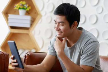 Evdeki kanepede oturup projeyi düşünürken düşünceli etnik erkek serbest yazar tableti karıştırıyor.