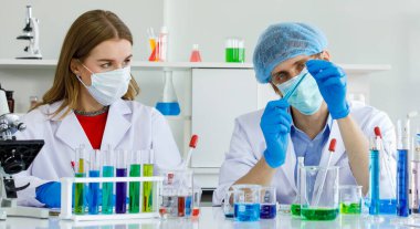 Beyaz erkek ve kadın bilim adamı test sonuçları hakkında tartışıyorlar. İnsan deney tüpü ve bilim aletleri mikroskobu tutar. Laboratuvarda bir sürü test tüpü bulunur..