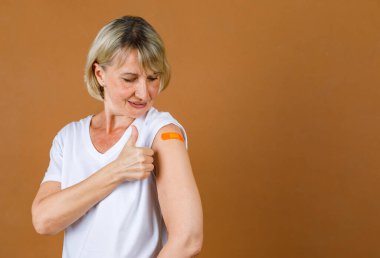 Kafkasyalı son sınıf sarışın kadının Coronavirus aşısı olduktan sonra omzundaki turuncu alçı bandaj başparmağının portresi..