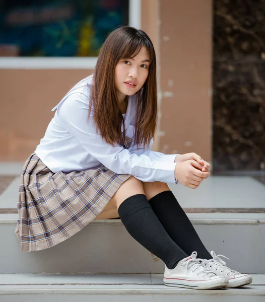 若い魅力的な女性のアジアの高校生の肖像白いシャツ茶色い小学校制服が学校のキャンパスに座っている — ストック写真