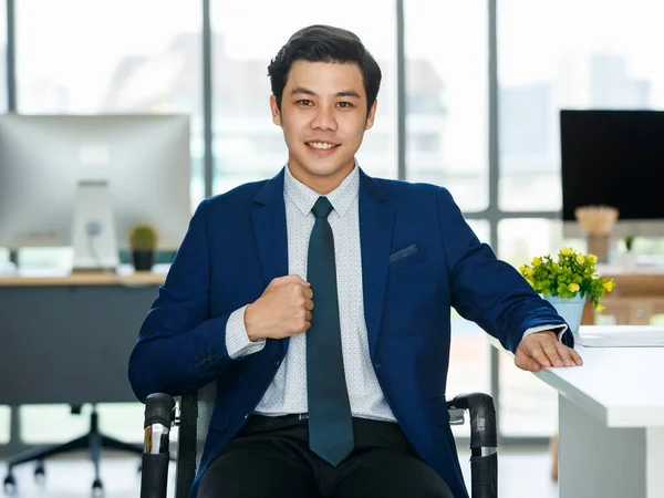 現代的なオフィスに座っている青のスーツで若いと優雅アジアのビジネスマンフレンドリーなポーズと自信を持って — ストック写真