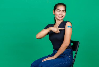 Koluna bandaj bandıyla gülümseyen orta yaşlı Asyalı kadın yeşil arka planda Covid 19 virüsü aşısı olduğunu gösteriyor. Covid 19 aşısı için kavram.