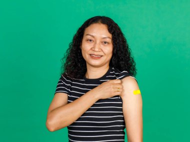 Kolunda bandaj bandı olan Asyalı orta yaşlı bir kadın yeşil arka planda Covid 19 virüsü aşısı olduğunu gösteriyor. Covid 19 aşısı için kavram.