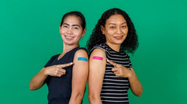 Kollarını bandajlı gösteren iki orta yaşlı Asyalı kadın yeşil arka planda Covid 19 virüsü için aşı olduklarını gösteriyor. Covid 19 aşısı için kavram.