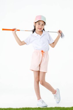Küçük sevimli Asyalı golfçünün, spor üniformalı ve yeşil çimlerin üzerinde durup turuncu saplı beyaz arka planda golf sopası sürücüsünün portresi..