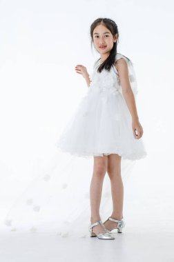 Küçük Asyalı şirin balerin çocuğun portresi. Yüksek topuklu güzel bale elbisesi içinde. Beyaz arka planda gülümseyerek zarif bir jest yapıyor..