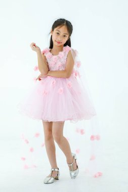 Küçük Asyalı şirin balerin çocuğun portresi. Yüksek topuklu güzel bale elbisesi içinde. Beyaz arka planda gülümseyerek zarif bir jest yapıyor..