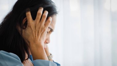 Orta yaşlı Asyalı kadın acı çekiyor ve ani baş ağrısı ve beyin felci krizinden muzdarip ve acı çeken yüzüyle başını tutuyor. Beyin ve kafa problemi kavramı.