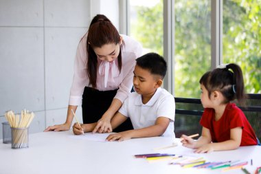 Asyalı kadın, güzel, yetenekli bekar anne, küçük ilkokul çocuğuna masada ödev yapmasını öğretirken, sevimli kız da yakınlarda çizim yapan renkli kalemleri gözlemliyor..