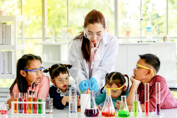 穿着白色实验室外套 橡胶手套和安全眼镜的亚洲女专业科学家教师在实验室用试管显微镜对小学男女学生进行科学实验 — 图库照片