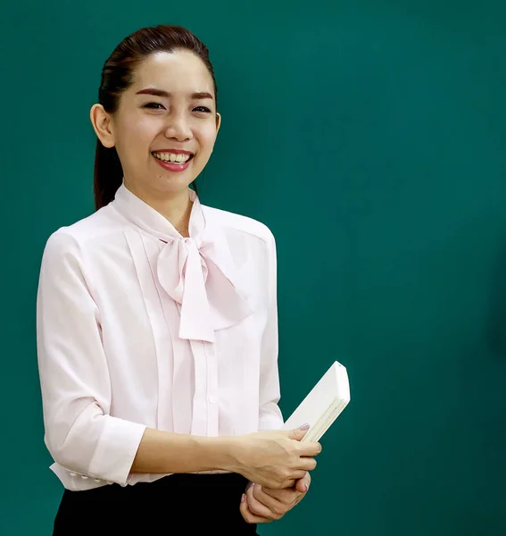 アジアの若い美少女先生のポートレート撮影教室で小学生に授業をしながら 手で教科書を持ってカメラを見て立って講師 — ストック写真