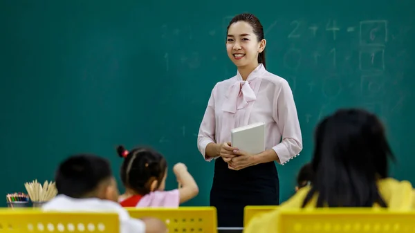 텍스트 아시아의 여교사 교실에서 초등학생들에게 강의를 하면서 카메라를 봅니다 — 스톡 사진