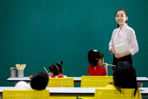 텍스트 아시아의 여교사 교실에서 초등학생들에게 강의를 하면서 카메라를 봅니다 — 스톡 사진