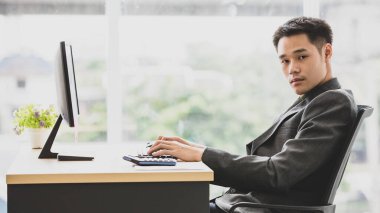 Resmi siyah takım elbiseli genç Asyalı iş adamı zarif görünüyor. Ofiste bilgisayarın önünde oturan, beyaz bir ses tonu. Yetenek ve kararlılıkla. Şirketin lideri olmayı hak ediyor.