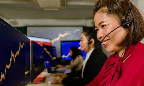 Teamwork of happy female trading marketing operators wears microphone headset sit smiling making bitcoin cryptocurrency stock exchange buy sell trading transaction from chart graph monitor in office.