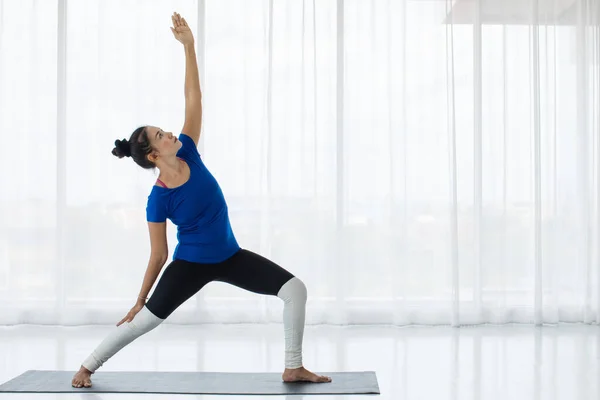 Young lady workout doing yoga by standing triangle shape right hand up to the sky and left touching leg concentration in deep breath, stretching muscle. This like practice meditation