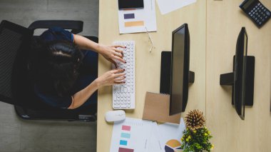 Profesyonel Asyalı bir iş kadınının ahşap masada oturup klavyeyle doküman yazarken çekilmiş üst görünüm portresi. Ofiste bilgisayar kullanarak çalışan bir kadın.