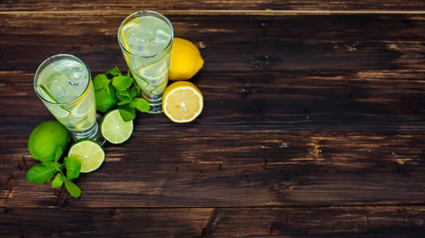 Tahta masada limon, limon ve naneli ev yapımı limonata bardaklarının düz görüntüsü. Resmin yanında metin yazmak için iki bardak kopyalanmış limonata var.