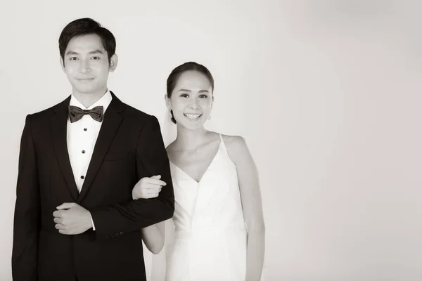 若い魅力的なアジアのカップル 花嫁と新郎 女性は白いウェディングドレスを着て 黒いタキシードを着た男が黒と白で腕を組んで立っている 結婚式前の写真のコンセプト — ストック写真