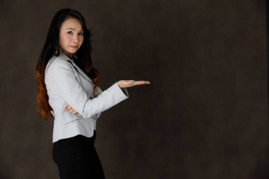 Zarif giysiler içinde zarif Asyalı genç bir iş kadını. Gülümsüyor ve gri arka planda boş alan gösteriyor.