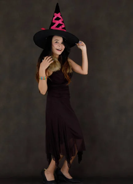 魅力的な若いですアジアの女性で魔術の衣装と帽子笑顔と暗い灰色の背景を背景にカメラを見て — ストック写真