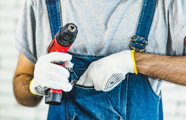 Küçük Asya adam holding matkap beyaz tuğla duvarın önünde, ayakta gülümseyen ve kamera, ev DIY için kavram bakarak