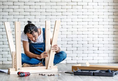 Tamirci olarak çalışan hippi genç adam, ahşap masayı teçhizat ve manüel ile birleştiriyor, ev yapımı için konsept ve arka planda beyaz tuğla duvar ile self servis..