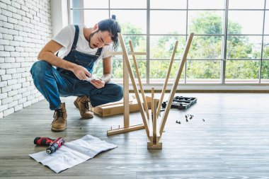 Tamirci olarak çalışan hippi genç adam, ahşap masayı malzemelerle birleştirmek için kullanım kılavuzu arıyor. Ev yapımı ve self servis kavramı. Ofiste..