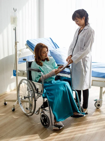 患者さんは車椅子に座って集中的に聴き入っていますが 医師が事故報告書では専門家のサポートで腕を骨折から回復する方法も説明しています — ストック写真