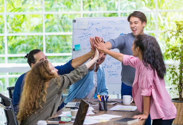 Çok ırklı iş adamları, takım çalışmasının birlik gücünü teşvik etmek ve motive etmek için ellerini bir araya getirerek, kapalı kapılar ardında modern ofiste dururken başarılı yaratıcı projeleri kutluyorlar.