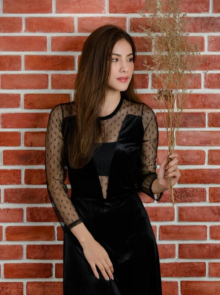年轻美丽迷人的亚洲女模特形象 身披黑衣 面带微笑地站在橙色砖墙的背景下 — 图库照片