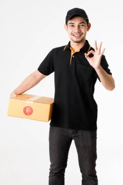 Gülümseyen Asyalı teslimatçı paketi sağ elinde tutarken iyi bir hareket yapıyor. İzole edilmiş beyaz arka planda siyah üniformalı kurye portresi. E-ticaret iş konsepti