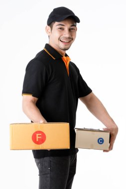 Neşeli Asyalı teslimatçı her iki elinde paketler tutuyor, kameraya gülümsüyor. İzole edilmiş beyaz arka planda siyah üniformalı kurye portresi. E-ticaret iş konsepti