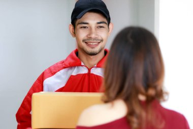 Gülümseyen Asyalı kurye evdeki Asyalı kadın müşteriye paket teslim ediyor. Paket teslimatı ve nakliyat, kapı kapı e-ticaret konsepti.