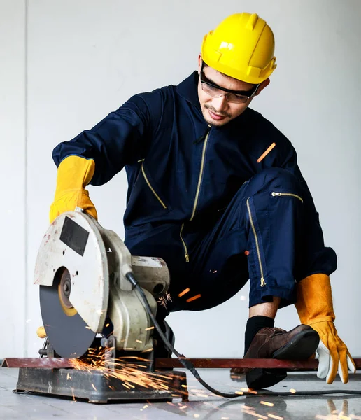 Odaklanmış genç Asyalı erkek işçi çelik kesme makinesinin yanında oturup çalışmaya hazırlanıyor. Atölye ve inşaat güvenliği kavramı