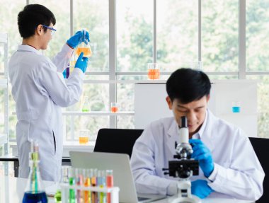2 Asyalı bilim adamı laboratuvar odasında kimyasal sıvıyla birlikte test tüpü üzerinde çalışıyor.