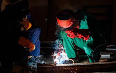 Tamirciler geceleri fabrikada fazla mesai yapmazlar. Tamirci tulumları, eldivenleri, botları ve metal kaynaklama kaskları olan güvenlik kıyafetleri giyen mühendisler..