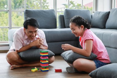 Mutlu kızı olan neşeli, genç Asyalı bir adam kanepenin yanında oturuyor ve hafta sonu evde kule oyunu oynuyor.