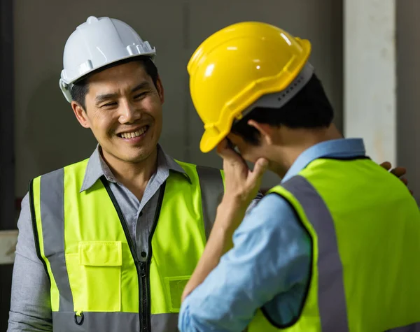 Senior and junior engineers talking together with intimated manner beside the machine in factory. Concept for good teamwork and unity of colleauges.