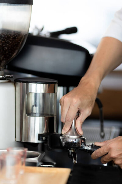 закрыть фотографию мужчин, держащих в руках металлический фальсификатор и портатор с кофе в кофейне. Мужчина-бариста готовит молотый кофе для варки эспрессо или американо в кафе