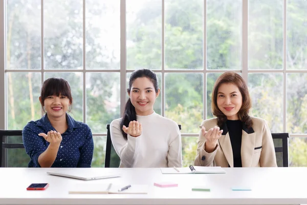 Three beautiful and self-confident businesswomen sitting in office and showing hand sign language skill in the same action.