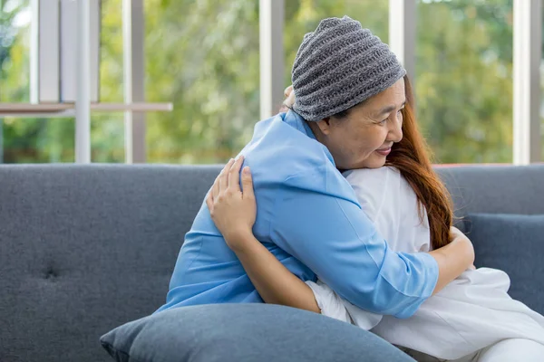 Older Asian woman patient covered the head with clothes effect from chemo treatment in cancer cure process hugging her daughter with love and happy.