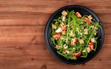 Domatesli taze roket salatası, çıtır ekmek, kavrulmuş küçük sebzeli tavuk parçaları ve siyah seramik tabakta parmesan peyniri..