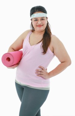 Asyalı mutlu, sağlıklı, spor giysili, kafa bandı takmış, gülümseyen, beyaz arka planda pembe yoga minderi tutarken çekilmiş bir portre resmi..