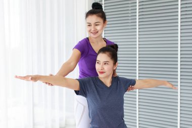 Savaşçı duruşu için öğrencinin arkasında duran ve spor salonunda ya da evde duruşunu düzelten kadın yoga eğitmeninin yan görünüm portresi.