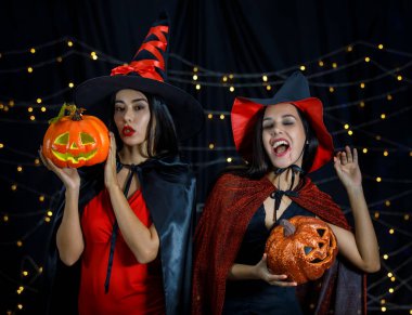 Cadı kıyafetleri içinde ve ellerinde balkabağı kafaları olan genç bayan arkadaşlar Cadılar Bayramı partisinde eğleniyorlar.