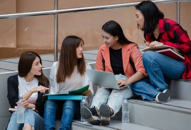 Dört çekici Asyalı üniversite öğrencisi üniversite kampüsündeki her merdivende oturup açık havada ders çalışıyor. Eğitim, arkadaşlık ve üniversite öğrencilerinin hayatı kavramı.