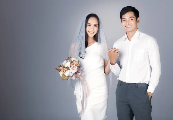 若い魅力的なアジアのカップルの手を握り 男性は白いシャツを着て 女性はベールの花の花束を保持して結婚式のガウンを着ての肖像画 結婚式前の写真のコンセプト — ストック写真