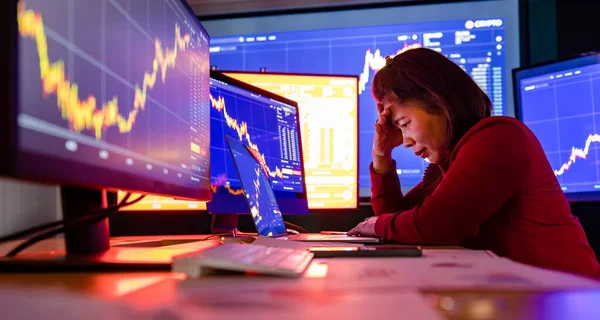 Başarısız komisyoncu, borsa değeri bilgisayar ekranı analizi raporundan düşerken ticaret odasındaki çalışma masasında stres altında oturur ve el ele tutuşur..