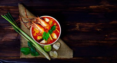 Taze lezzetli Tom Yam Kung sıcak tatlı ekşi Tayland baharatlı karides mantarı ve beyaz klozette sebze çorbası ve ahşap masaya soğan ve fesleğen..